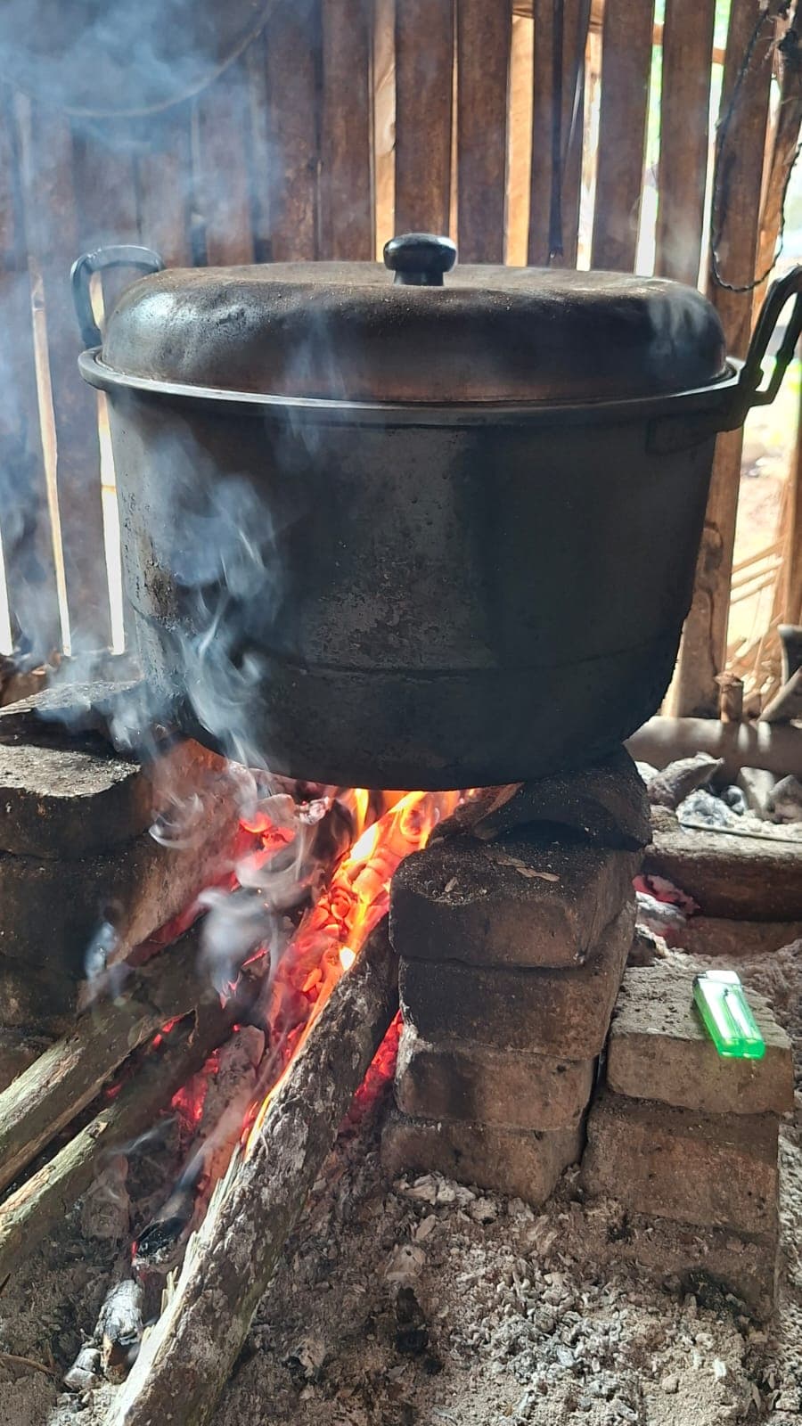 Panci besar mengukus di atas bara kayu bakar.