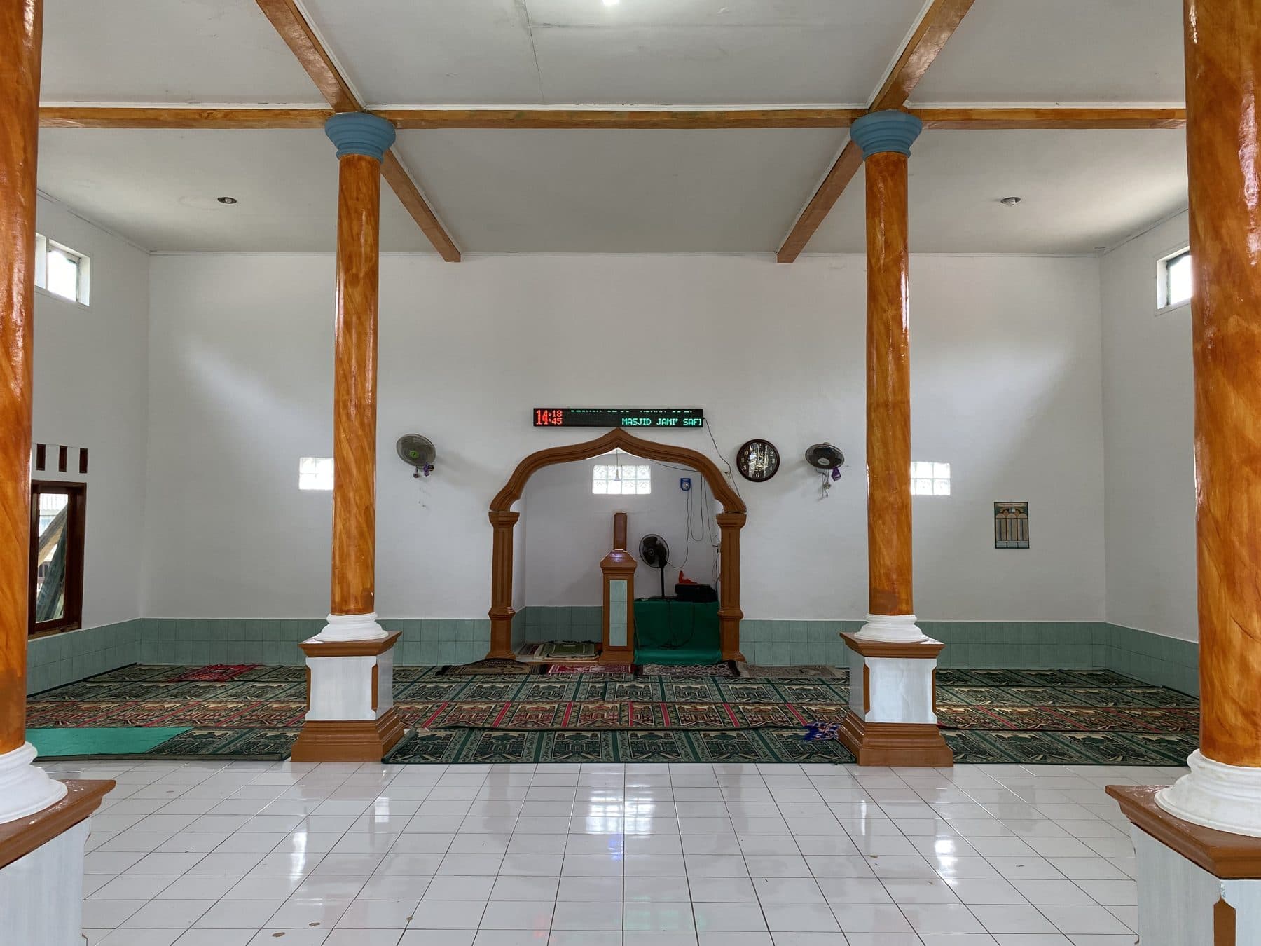 Ruang shalat masjid yang lapang dengan tiang kayu dan hamparan sajadah di Desa Tembong.